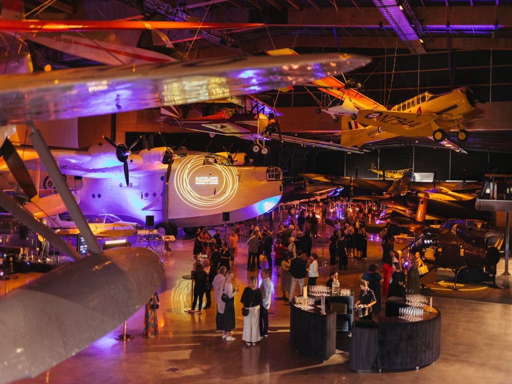 Guests gather at an event in the MOTAT aviation hall, with planes in the background and a bar setup in the foreground.