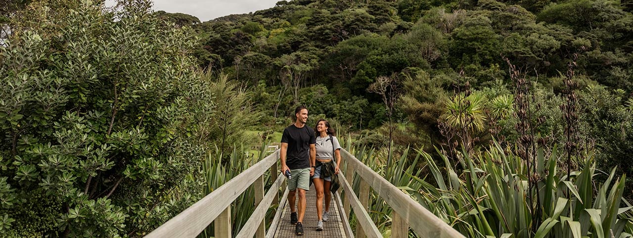 A couple walking on a bridge in native forest at Bethells Te Henga in west Auckland