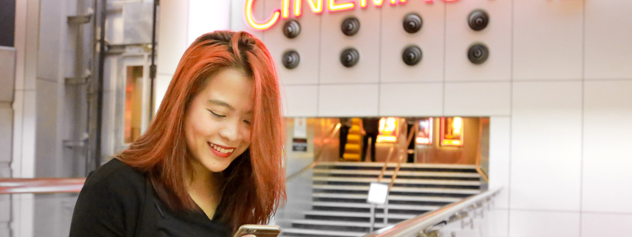 Person with pinky peach hair looking at phone and smiling