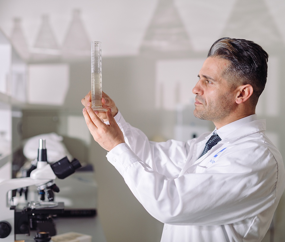 Lab technician in front of a microscope measuring liquid