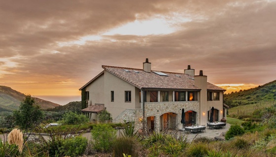 Mediterranean-looking loge set in rolling hills and ocean at sunset